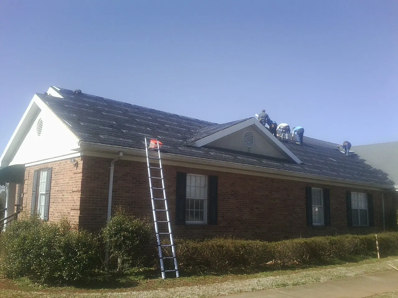 Crew tearing shingles off a brick ranch roof with a ladder set — Emergency Roof Repair work by our crew in Mansfield